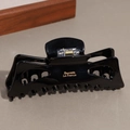 Detalle de pinza para el pelo negra brillante con texto dorado y resorte metálico - Grande / Negro