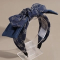 Detail van een denim blauwe haarband met grote strik en zilveren letterpatronen op een houder - Strikstijl