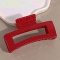 Close-up of a glossy red rectangular hair claw clip with hollow geometric design on a plate - Red