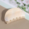 Detalle de una pinza de pelo de media luna grande con textura de mármol crema y dientes - Blanco Roto