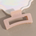 Detail shot of a square hollow hair claw clip in soft nude pink on a pearl tray - Beige