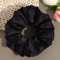 Detailed view of premium black satin scrunchie with glossy pleated texture and soft luster - Black