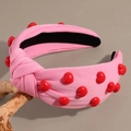 Close-up of pink padded headband with red 3D hearts and twisted knot on wood branch - Pink