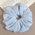 Detail of light blue pleated hair scrunchie with a Hand Made label on a soft background - Blue