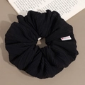 Detail of black pleated scrunchie with handmade heart label and elegant fabric texture - Black