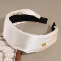 Detail van een crème satijnen hoofdband met gouden knoop en elegante geplooide stof - Broken Wit
