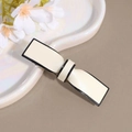 Detail van een crèmekleurige strik haarclip met zwarte rand op een plateau - Beige