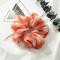 Detail eines orange-weißen karierten Scrunchies auf Stoff mit Eukalyptusblättern - Netz Orange