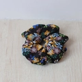 Nahaufnahme eines schwarzen Scrunchies mit buntem Blumenmuster auf hellem Holzgrund - Blumig Schwarz Blau