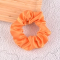 Close-up of bright orange satin scrunchie showing smooth silk texture and folds - Orange