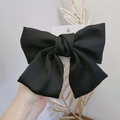 Detailed view of a large black satin bow hair clip held against a minimalist background - Black Bow