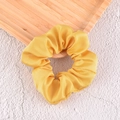 Detailed texture of a bright yellow satin scrunchie resting on a stylish wooden tray - Yellow