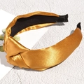 Detailed view of a golden satin headband with a twisted knot design on a stone surface - Gold
