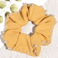Close-up of bright yellow fabric scrunchie with embedded white pearls on white background - Yellow