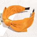 Detail of a shiny orange satin headband with a large bow on a white marble background - Orange