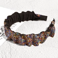 Dettaglio del cerchietto plissettato con strass colorati su sfondo materico - Pavé Colorato