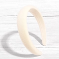 Cerchietto imbottito beige con trama in maglia morbida su sfondo di legno bianco - Bianco Sporco