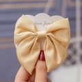 Detailed view of champagne satin fabric bow clip with silky texture on card - Yellow