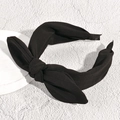 Detailed view of the knotted black bow headband on a textured white display stand - Black