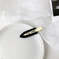Detail view of a matte black duckbill hair clip with golden metal accents on a ceramic tray - Milk Coffee Black