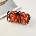 Détail d'une pince à cheveux en résine ambrée au design en spirale sur fond de magazine - Ambre