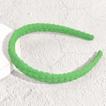 Dettaglio di un cerchietto verde smeraldo con trama a nido d'ape su supporto circolare - Verde Sottile