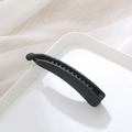 Close-up of matte black banana hair clip with internal teeth on a white decorative tray - Regular Fit / Black