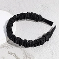 Detalle de la diadema de satén plisado negro sobre un fondo con textura elegante y lisa - Negro