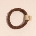 Détail du chouchou en peluche marron foncé avec un patch de lapin sur une surface texturée - Marron
