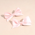 Close-up of two pink satin bow hair clips with soft lighting on a pastel background - Pink