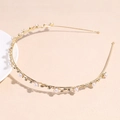 Dettaglio del cerchietto dorato con perle bianche e strass scintillanti su sfondo materico - Perla Strass Foglia
