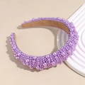 Detalle de diadema acolchada morada con perlas sobre un soporte de exhibición blanco - Morado