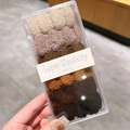 Détail d'élastiques à cheveux tons terre dans une boîte transparente avec texture de tissu - Dégradé café