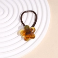 Detailed macro view of an amber resin flower hair tie on a white pedestal display - Amber