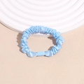 Close-up of light blue satin scrunchie with soft silk luster and pleated texture - Blue