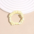 Close-up of a pale yellow pleated satin scrunchie with a sleek plastic connector detail - Yellow