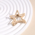 Macro detail of star-shaped matte hair claw clip in light brown on a textured display - Khaki Star