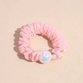 Dettaglio di un elastico in organza rosa con volant e perla iridescente su fondo beige - Rosa