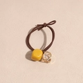 Dettaglio di un elastico per capelli marrone intrecciato con perla gialla e pendente dorato - Giallo
