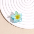 Macro detail of blue plumeria hair claw clip with yellow gradient on a beach textured tray - Blue