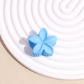 Gros plan d'une pince à cheveux fleur bleue mate sur un plateau de présentation blanc - Bleu