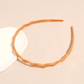 Close-up of orange wavy headband with inner teeth design on minimalist background - Turmeric