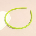 Close-up of bright neon green wavy headband with anti-slip teeth on a soft pink background - Grass Green