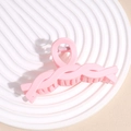 Detailed macro view of a large pink matte shark hair claw clip on a white pedestal - Pink Braided Twist
