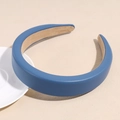 Dettaglio del cerchietto imbottito in ecopelle blu con fodera antiscivolo su superficie beige - Blu