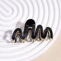 Detail of elegant black and gold wave hair claw clip on white textured tray - Black