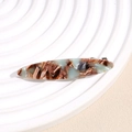 Close-up of leopard print hair clip with gold logo on a white textured plate - Brown Green