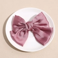 Detailed macro view of a dusky pink satin bow hair clip on a white ceramic plate - Pink
