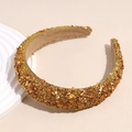 Dettaglio di pietre dorate e strass luccicanti su un cerchietto imbottito in stile retrò - Oro