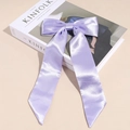 Dettaglio del fermaglio per capelli in raso lavanda con nastri lunghi su libro - Viola